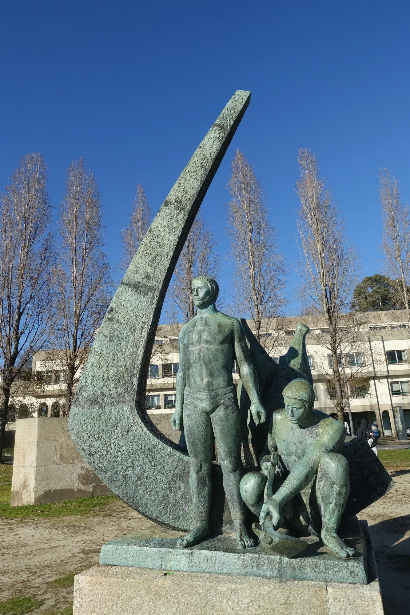 Monumento «Pela Grei» no Porto, dedicado a quem equipou a frota de 1415: um jovem construtor naval de pé e outro agachado a trabalhar, diante da proa curva de um barco.